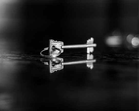 Artistic black and white photo capturing a key's reflection on a glossy surface, evoking mystery.